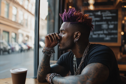 Stylish man with vibrant purple and orange dyed hair gazing out a coffee shop window, showcasing modern urban fashion and creative hair color trends.